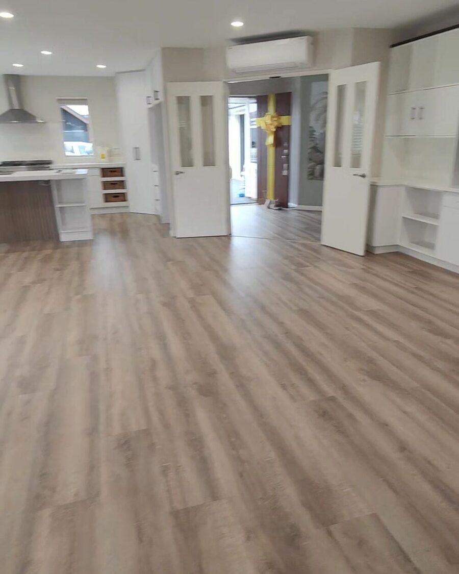 An emptied New Zealand home after a removal — bare timber-look floors, an open kitchen and a heat pump on the wall