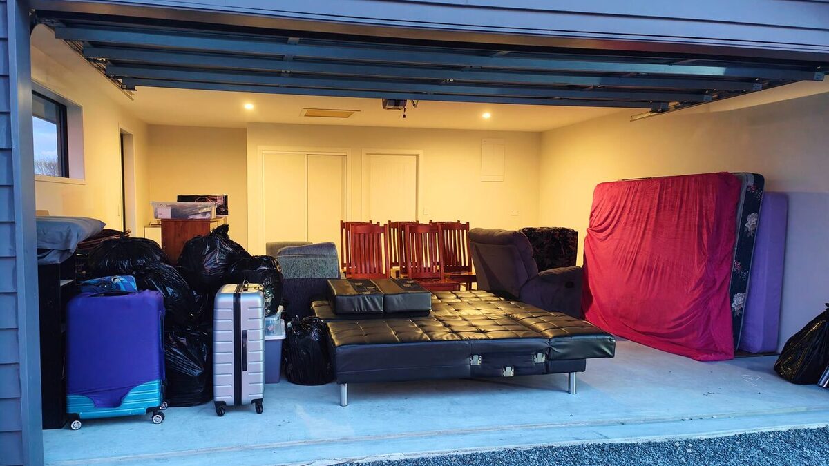 A household stacked ready to load in an open garage — bags, suitcases, dining chairs and mattresses for a house removal