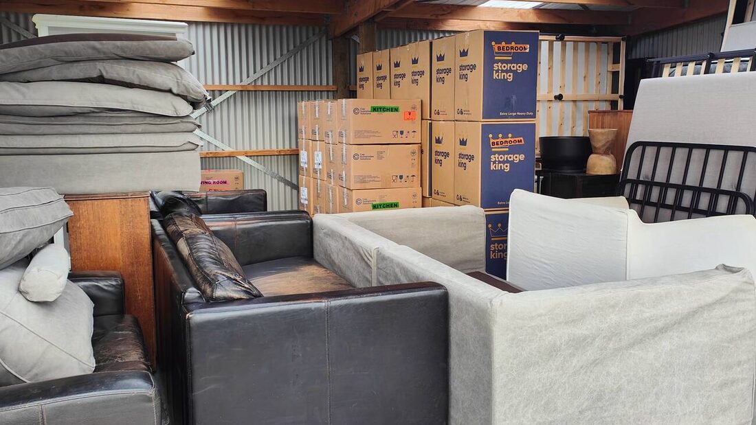 A timber shed packed floor to ceiling with a household removal — sofas, mattresses and stacked moving boxes under the trusses