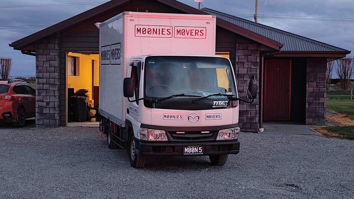 Moonies Movers' white removal truck on the gravel drive of a rural Canterbury house at dusk