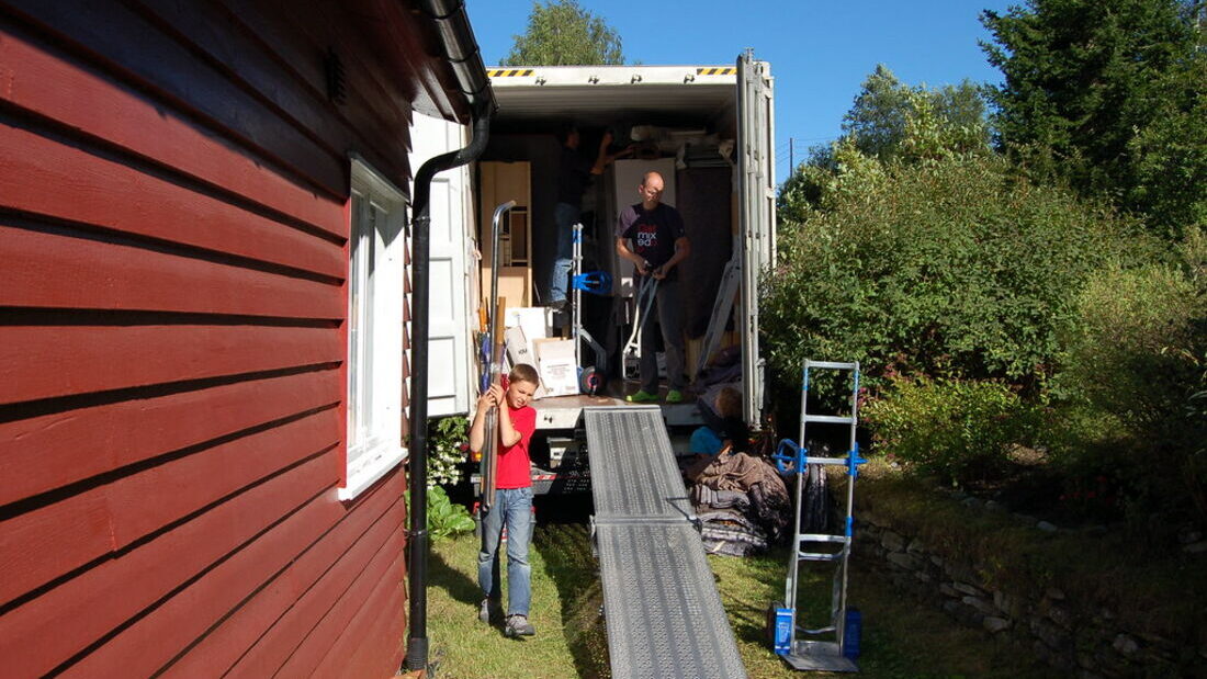A removalist working a hand truck inside the open back of a removal truck with the ramp down, beside a timber house