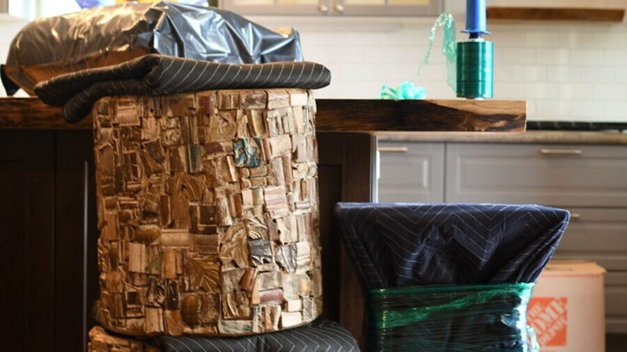 Kitchen stools and an armchair wrapped in moving blankets and stretch film, packed and waiting on a kitchen island